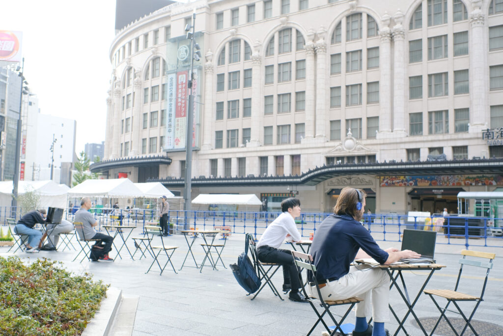 なんば広場で利活用エリア②の社会実験で設置した机椅子で仕事をしてる人の様子
